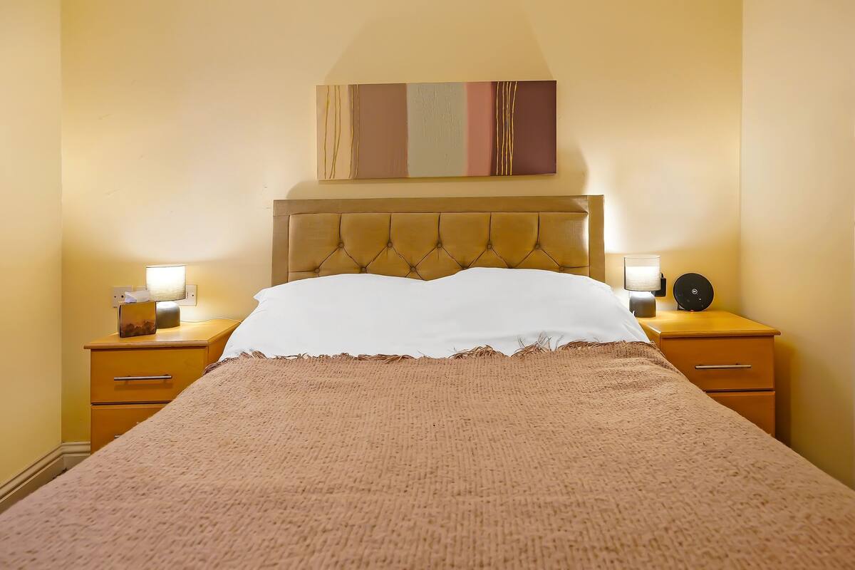 A neatly made bed with a tufted headboard, two bedside tables with lamps, and a painting above the bed.
