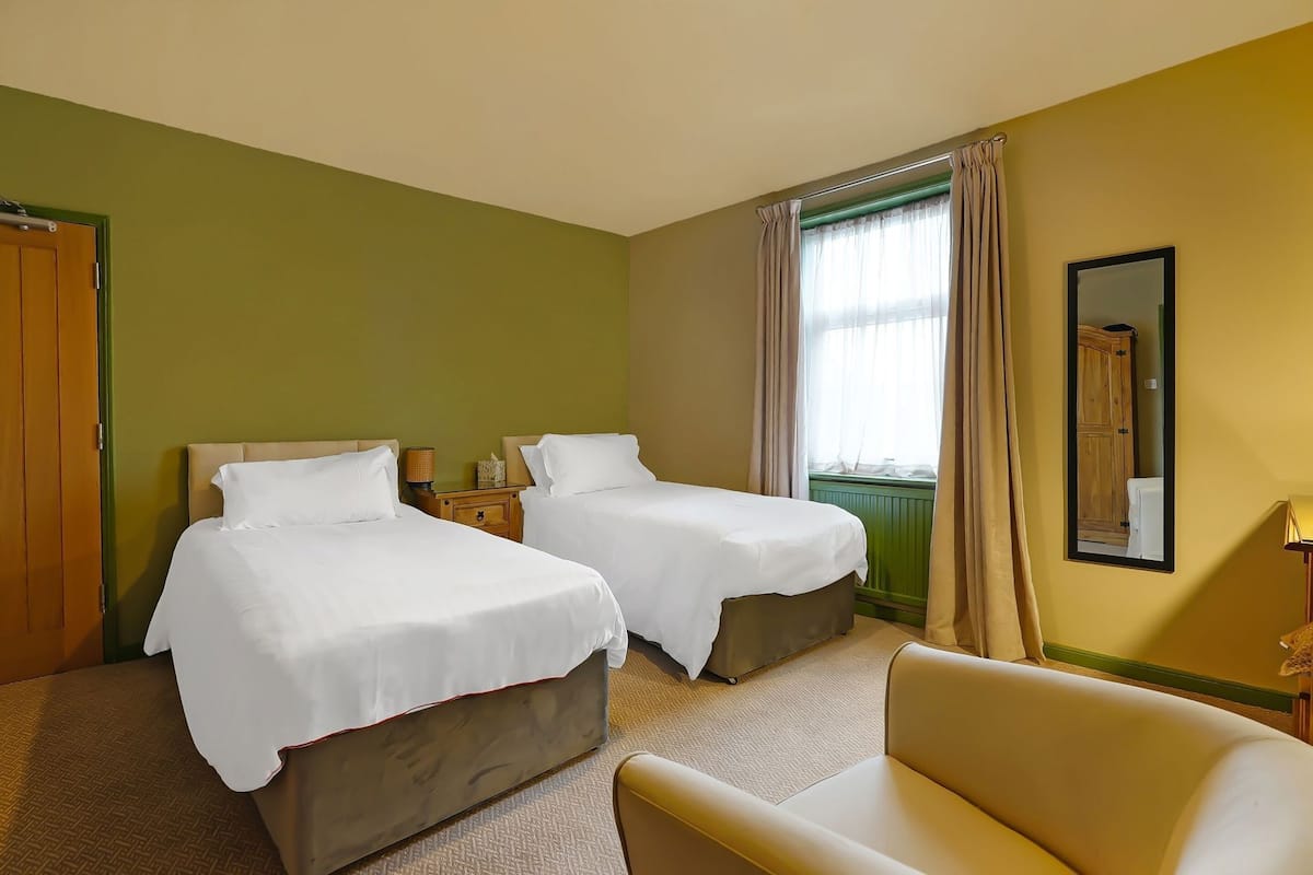 A hotel room with two beds, a sofa, a mirror, and a window with curtains.