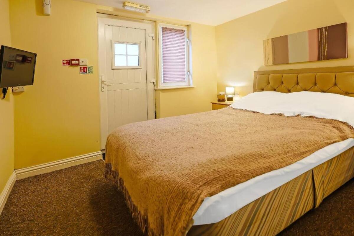 A hotel room with a bed, a television, a door, and a window with blinds.