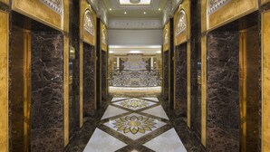 A luxurious hallway with marble floors, ornate gold detailing, and a grand chandelier.
