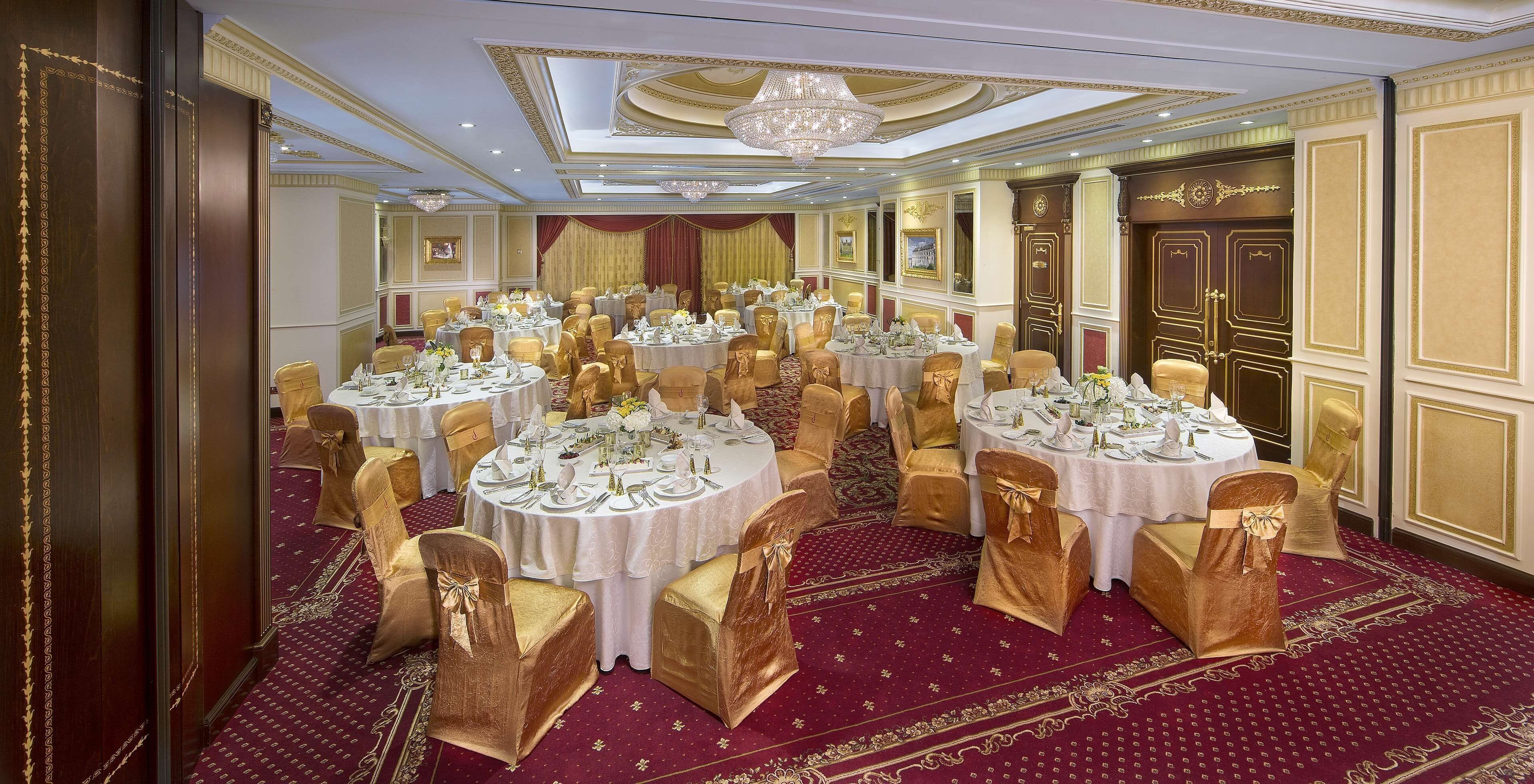 A banquet hall with round tables, gold chairs, and red carpets.