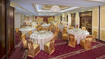 A banquet hall with round tables, gold chairs, and red carpets.