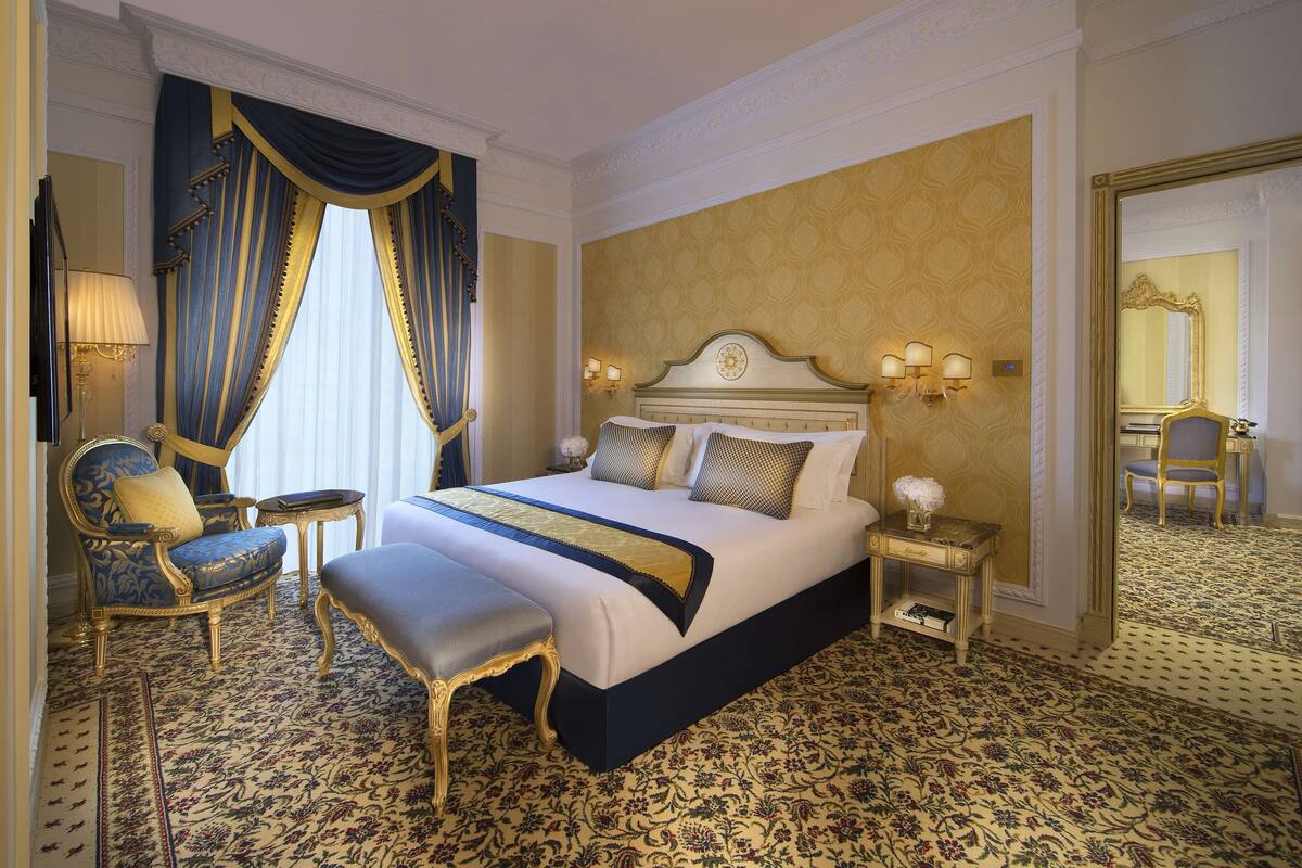 Een luxe hotelkamer met een groot bed, sierlijke gordijnen, een bijpassende fauteuil, een klein tafeltje en een spiegel.