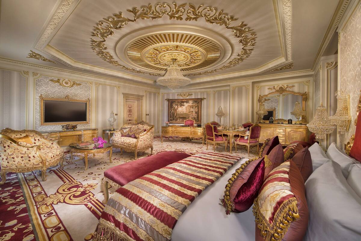 Een luxe kamer met decoratief plafond, een groot bed en een bureau met stoel.