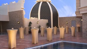 A pool area with a central dome structure, surrounded by beige pillars and a clear sky.