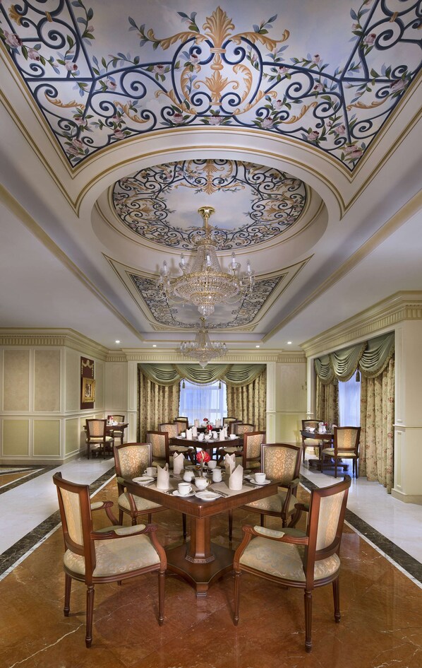 A grand dining room with a large chandelier, ornate ceiling, and a round table surrounded by chairs. - Royal Rose Hotel Abu Dhabi, Curio Collection by Hilton (Abu Dhabi)