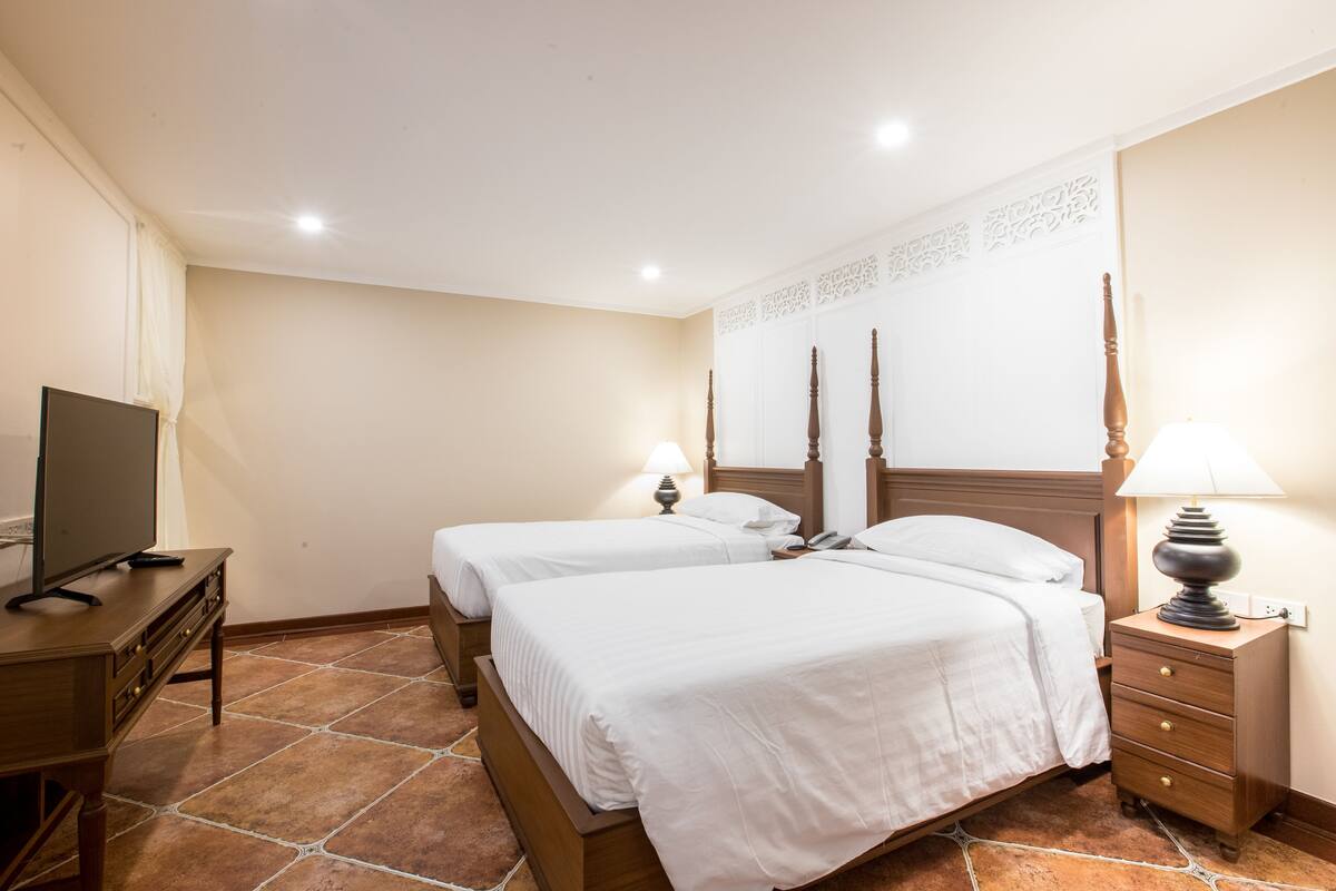 A hotel room with two beds, a television, a nightstand with a lamp, and a decorative wall panel.