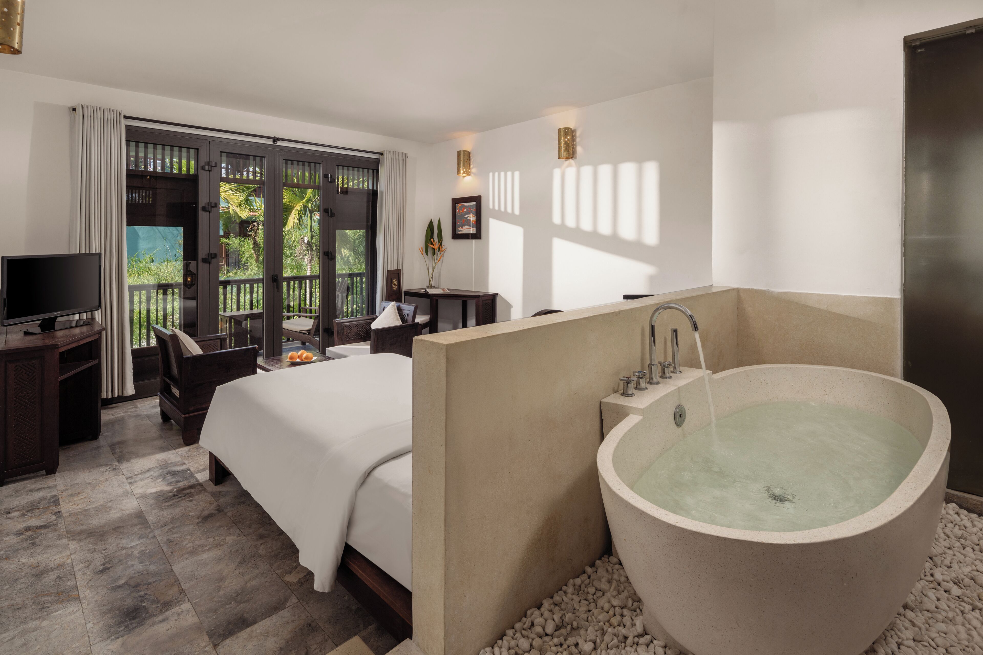 Une chambre d’hôtel dotée d’un grand lit, d’un coin salon, d’un bureau avec une télévision et d’une baignoire sur pieds.