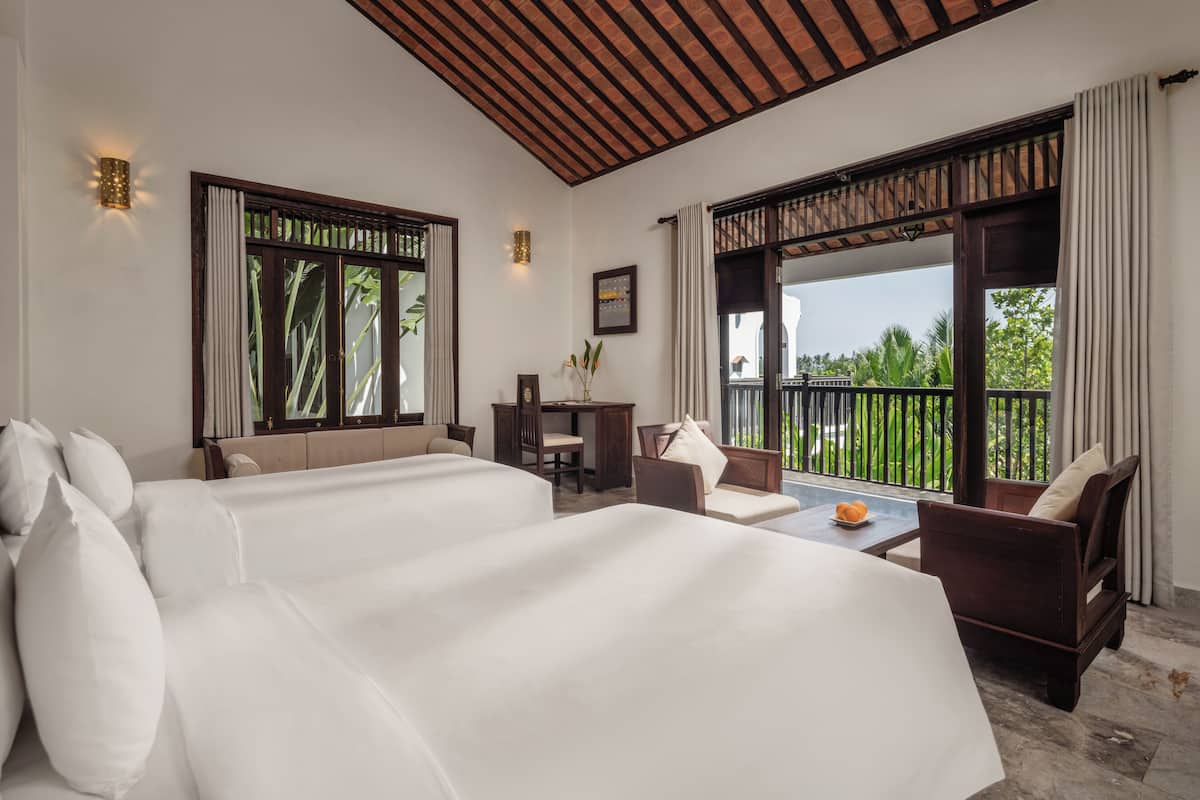 A hotel room with two beds, a desk, and a balcony with a view.