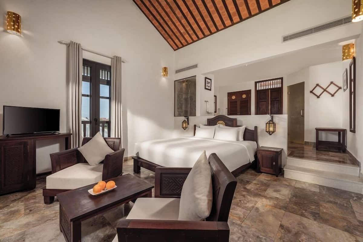 A hotel room with a large bed, a TV, a sofa, a coffee table, and a desk.