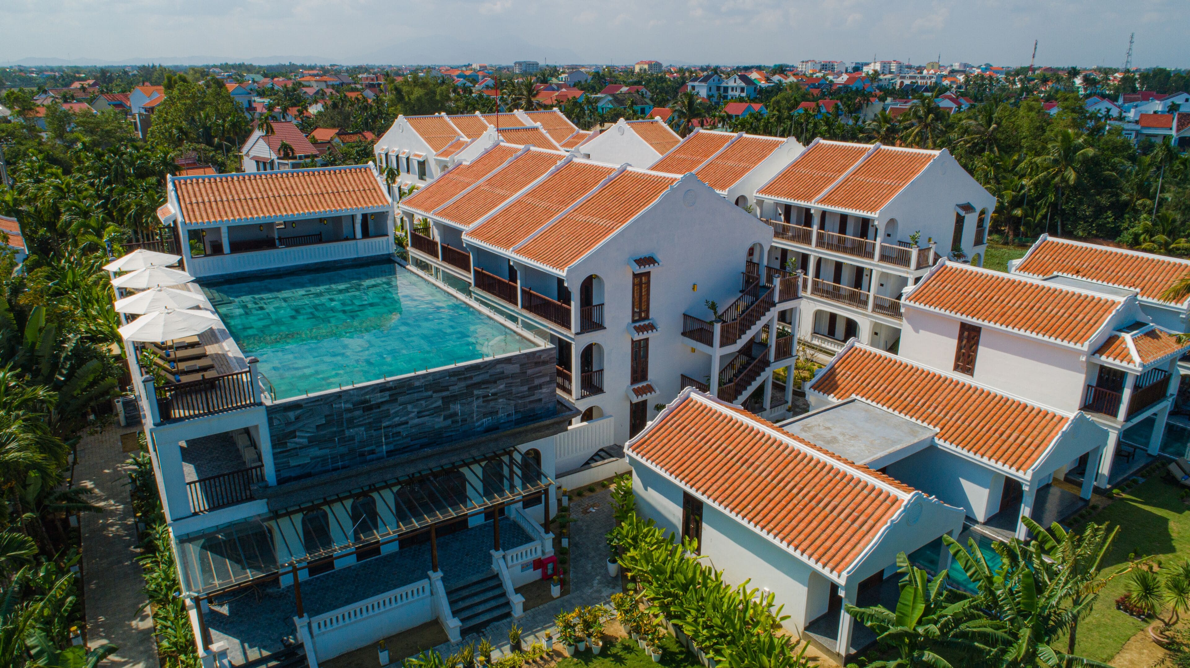 A resort with multiple buildings, a central swimming pool, and surrounding greenery.
