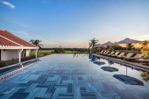 A swimming pool with a geometric tile pattern, lounge chairs, umbrellas, and a view of the surrounding landscape.