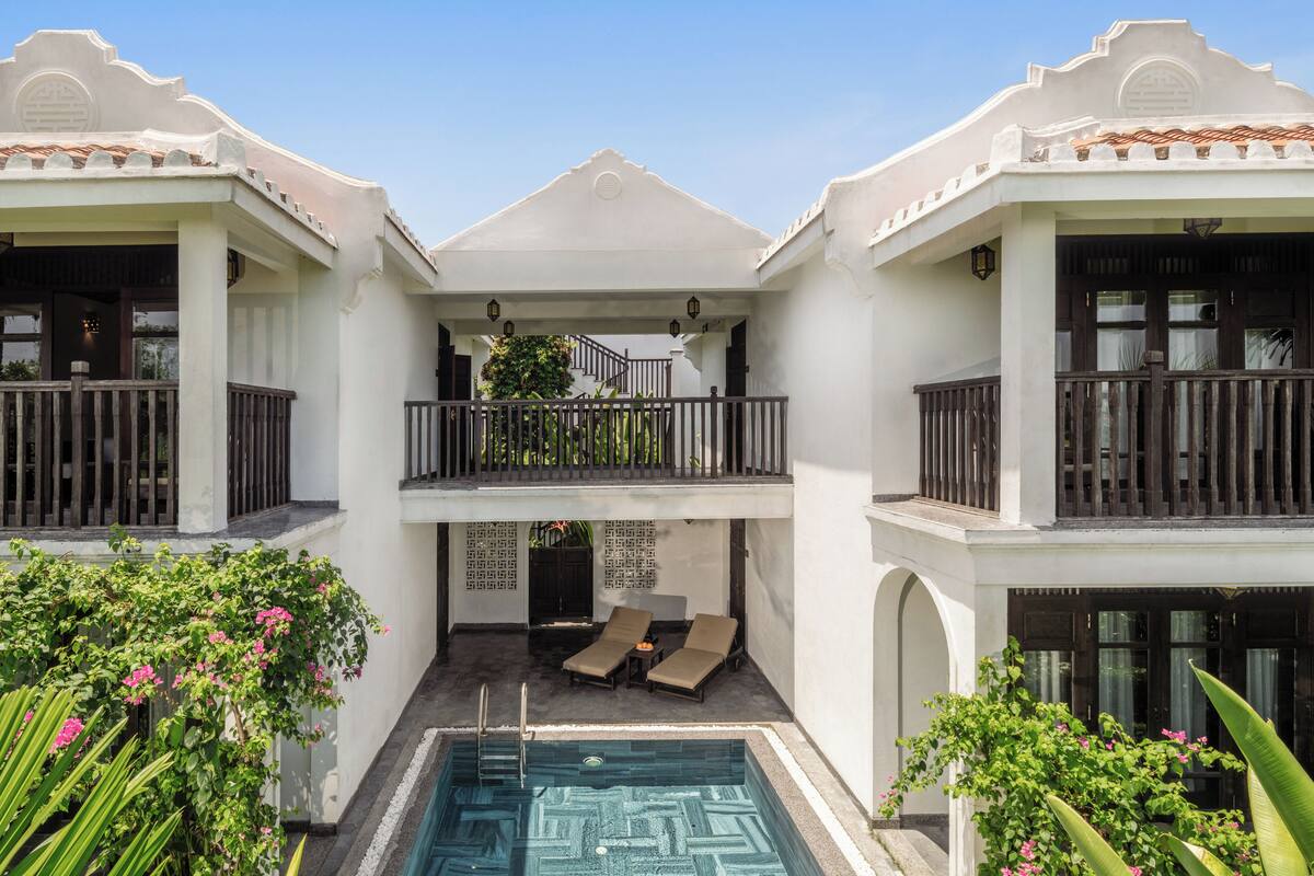 A two-story building with a central courtyard featuring a swimming pool, lounge chairs, and a staircase leading to an upper balcony.