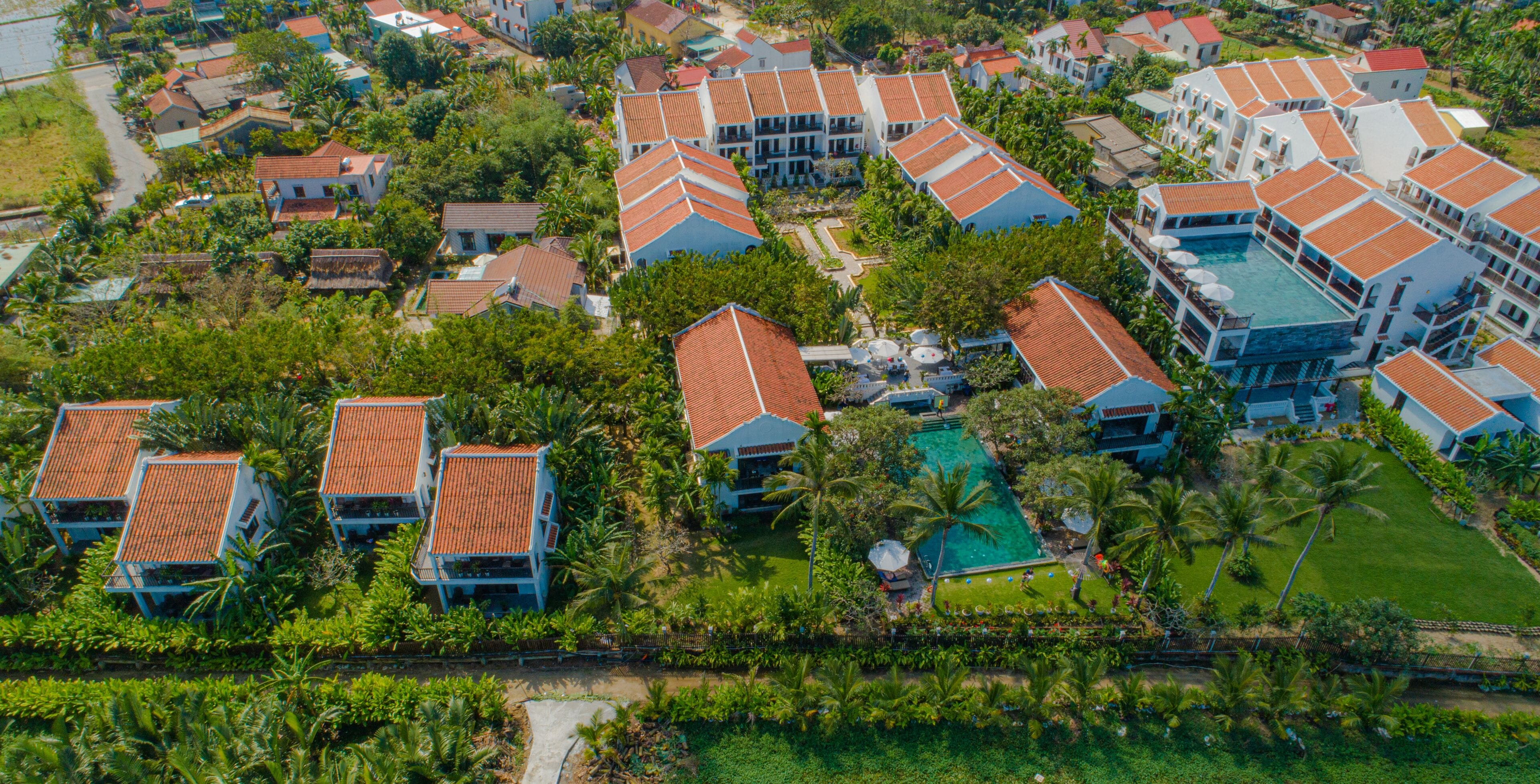 An aerial view of a resort with multiple buildings, a swimming pool, and lush greenery.