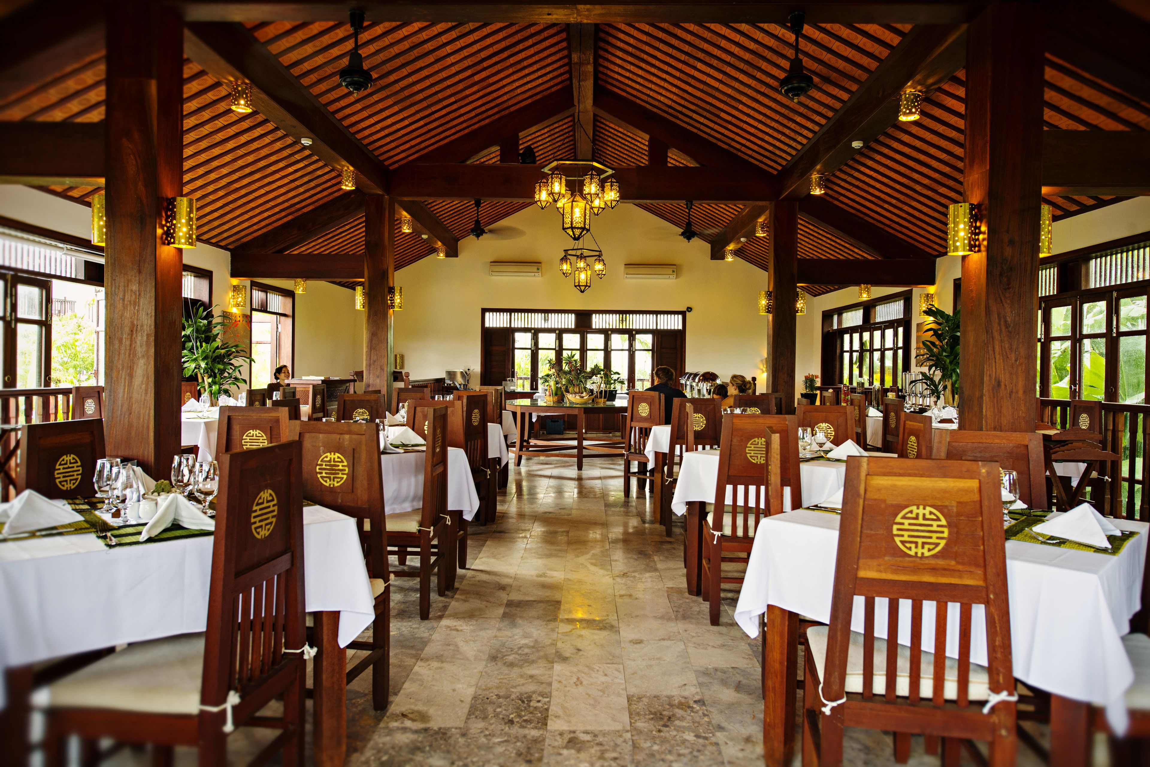 A restaurant with wooden tables and chairs, a tiled floor, and a chandelier.