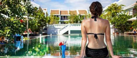 A person sitting by a pool with a drink on the edge.