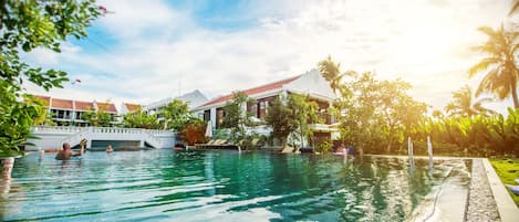 A swimming pool with clear water, surrounded by lush greenery and a building with a red roof.