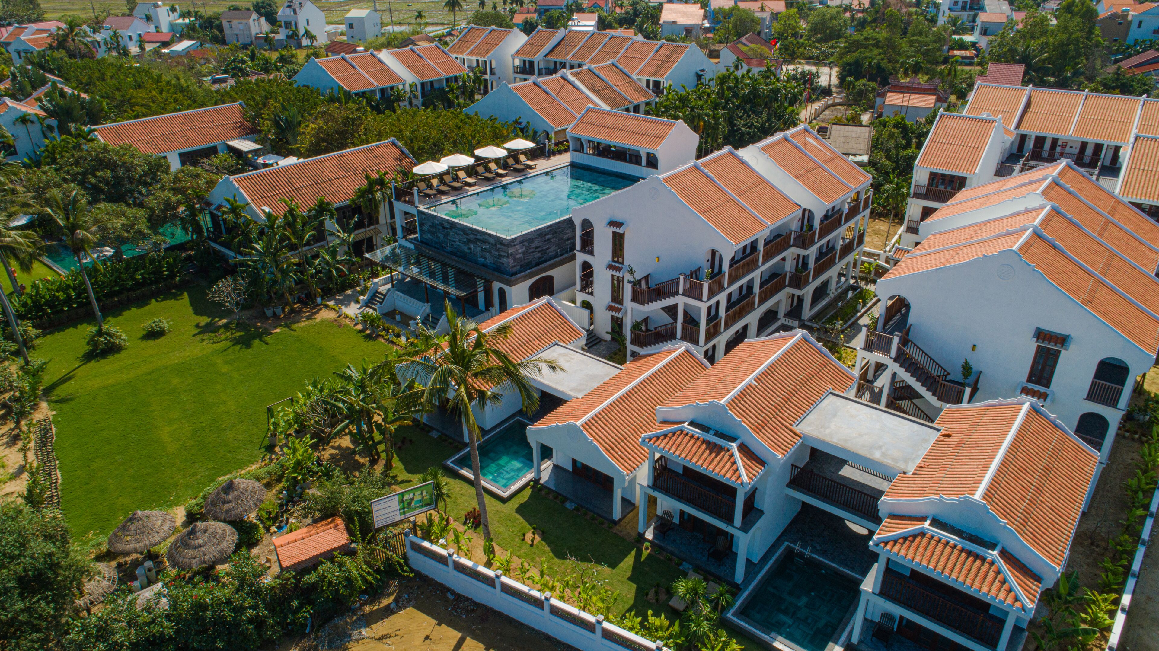 A resort with multiple buildings, a central swimming pool, and surrounding greenery.