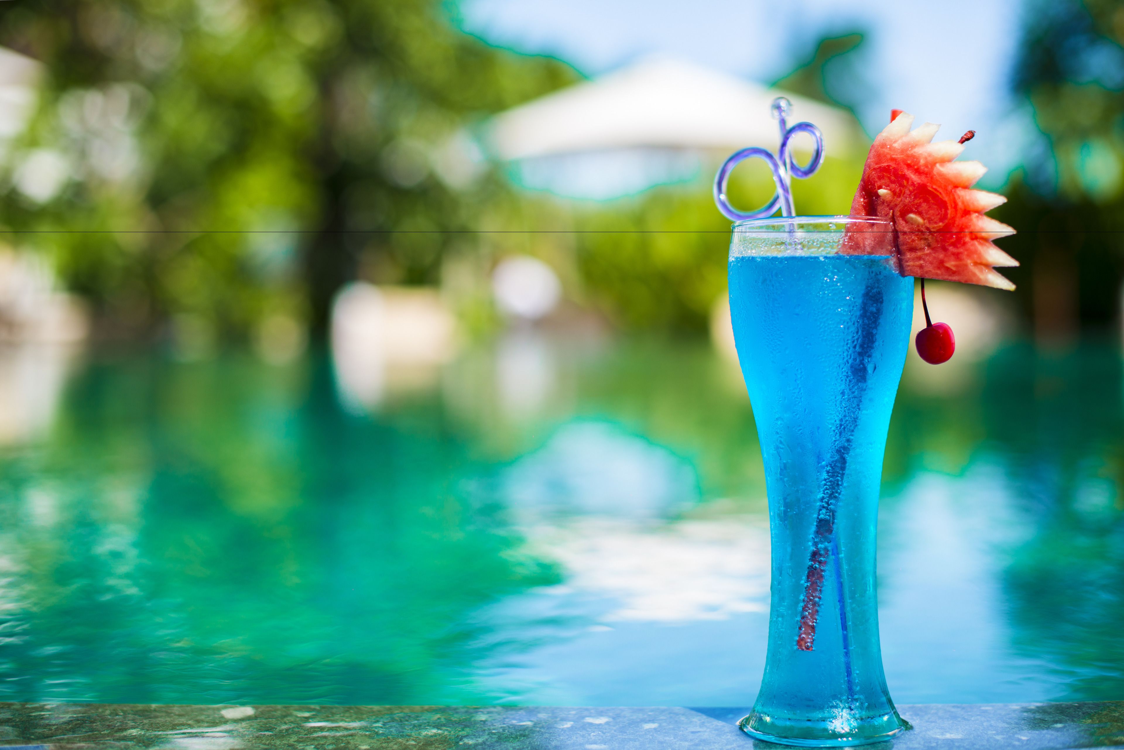 Ein hoher Glas mit einem blauen Getränk, einer dekorativen Frucht und einer Kirsche am Spieß.