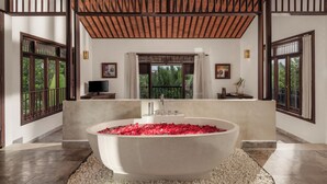 A spacious bathroom with a freestanding bathtub filled with rose petals, large windows, and a wooden ceiling. - Legacy Hoi An Resort (Da Nang)