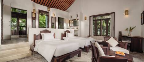 A spacious bedroom with three beds, a seating area, and a view of greenery.