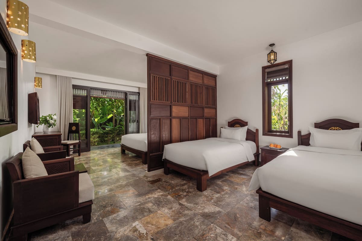 A hotel room with two beds, a seating area, a large window, and a view of greenery.