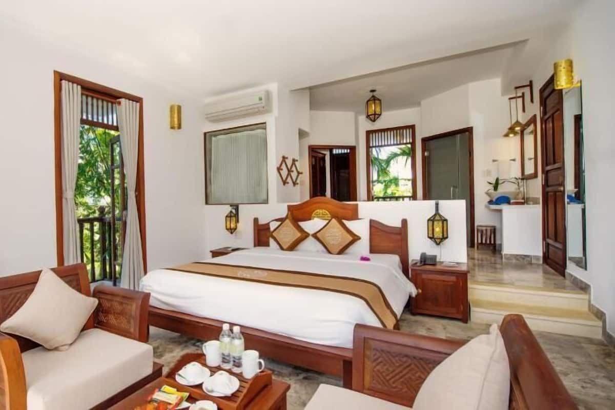 A hotel room with a bed, two wooden chairs, a small table with breakfast items, and a view of the outdoors.
