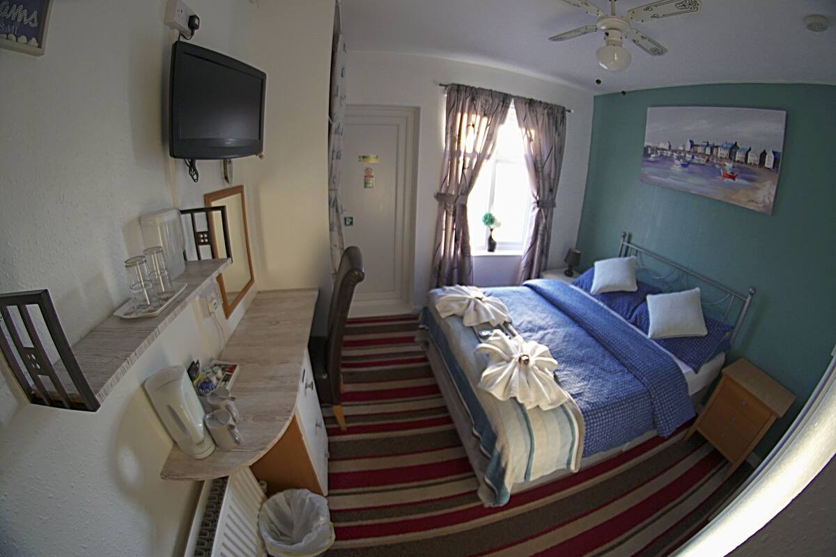 Een hotelkamer met een bed, een bureau, een televisie en een raam met gordijnen.