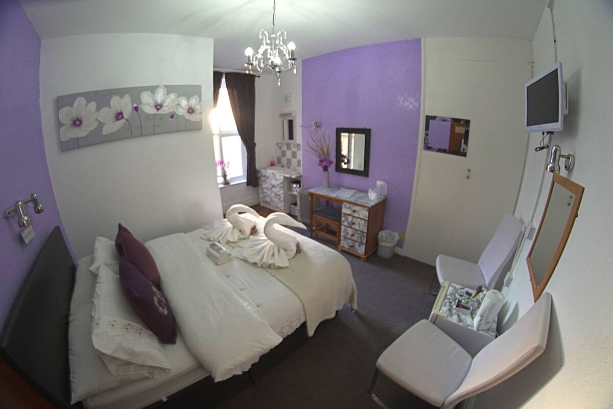 Een slaapkamer met een bed, een stoel, een dressoir, een televisie en een spiegel.