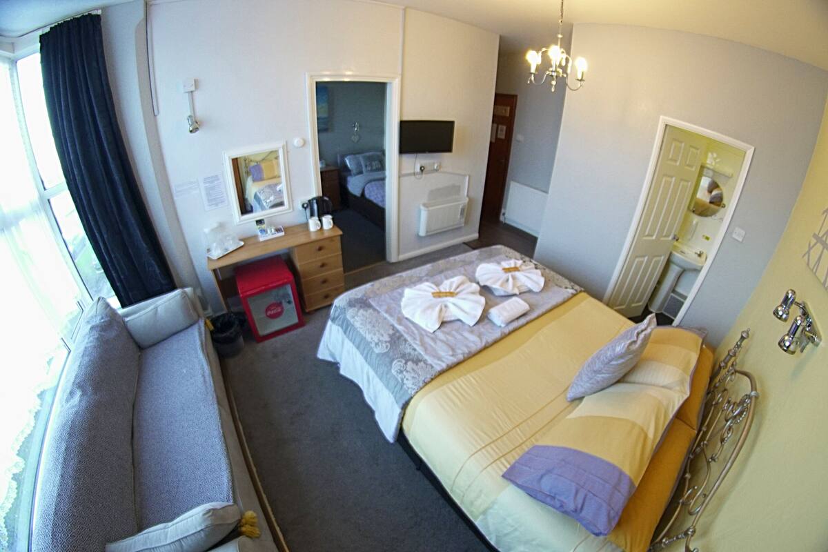 Een hotelkamer met een bed, een slaapbank, een bureau, een spiegel, een televisie en een badkamer.