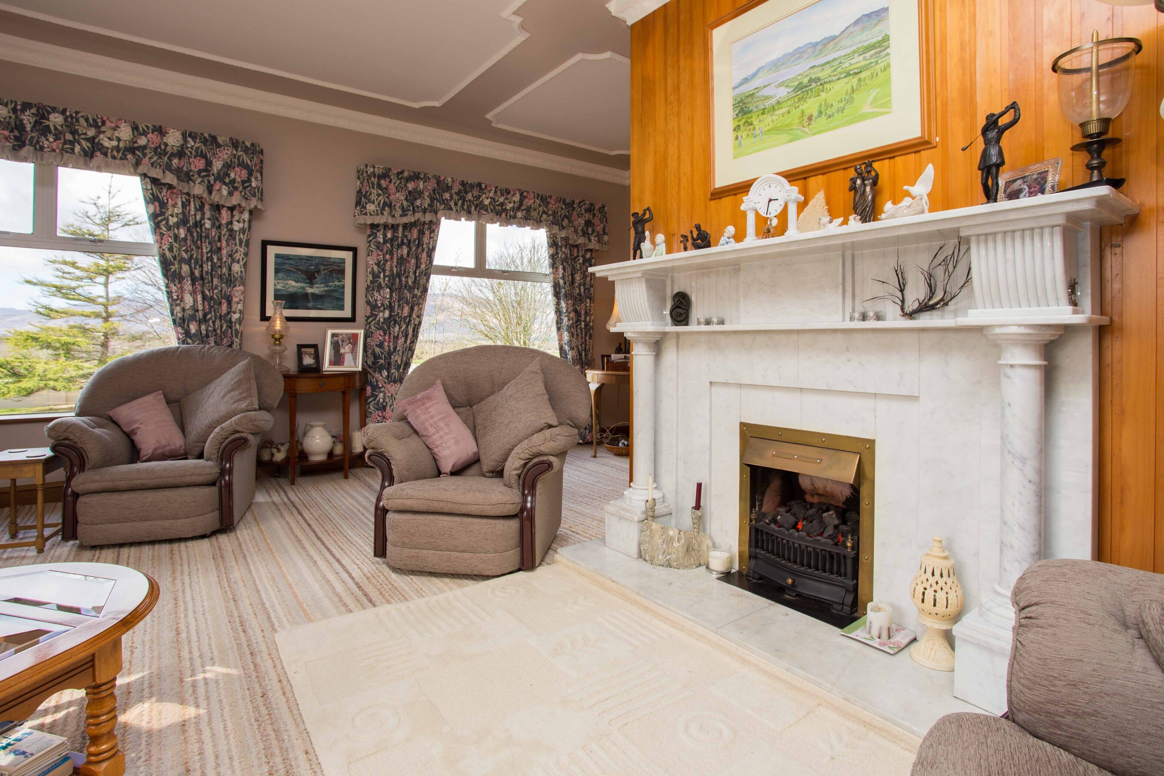 A cozy living room with two armchairs, a fireplace, and a large window with floral curtains.