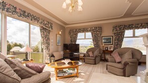 A living room with a sofa, armchair, and a coffee table with books. There is a TV and a fireplace. - Fern Rock B&B (Milltown)