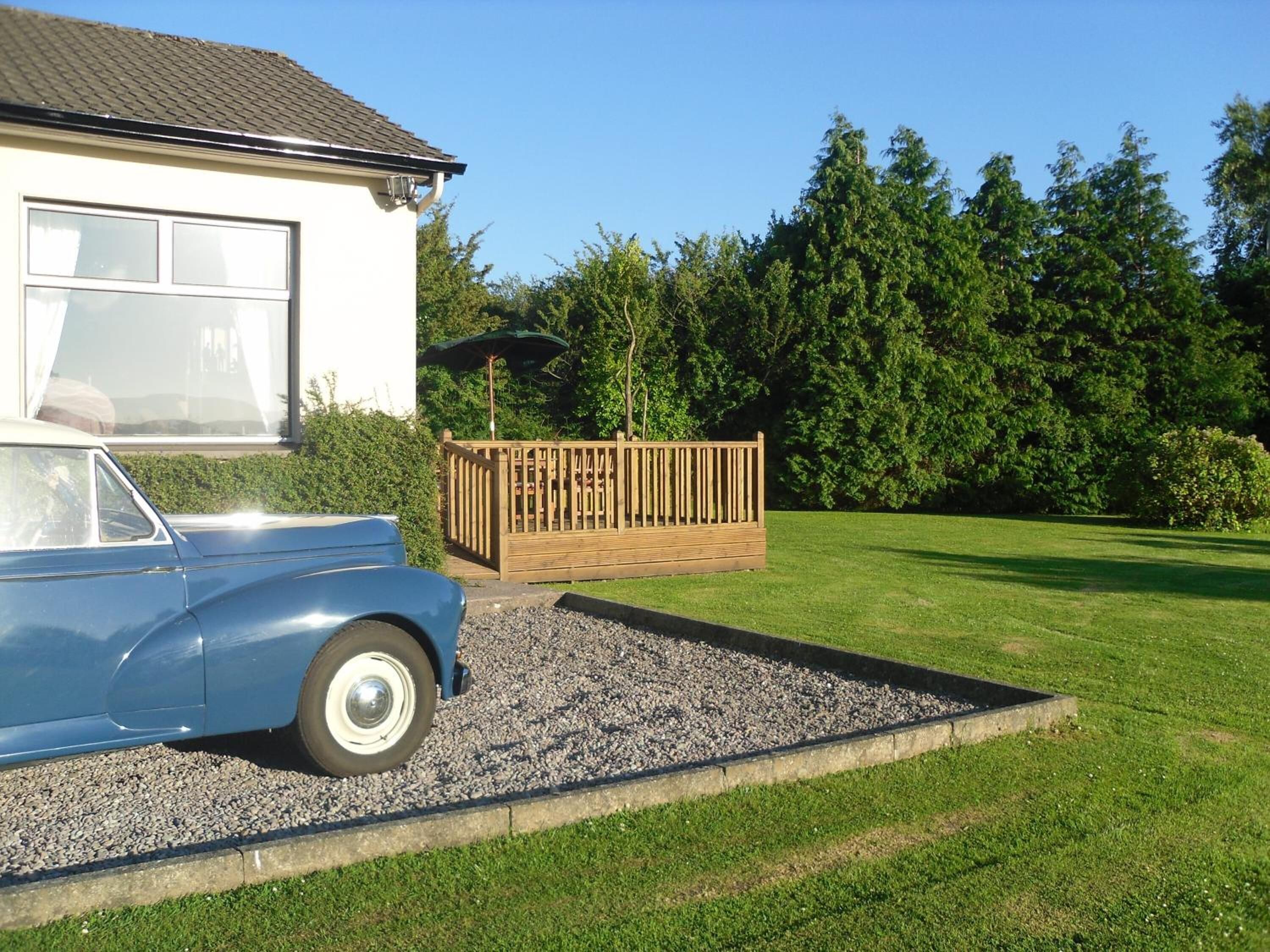 A house with a blue car parked in front, a wooden fence, and a grassy yard.