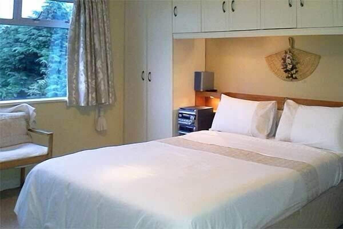 Un dormitorio con cama, una silla, un escritorio y una ventana con cortinas.