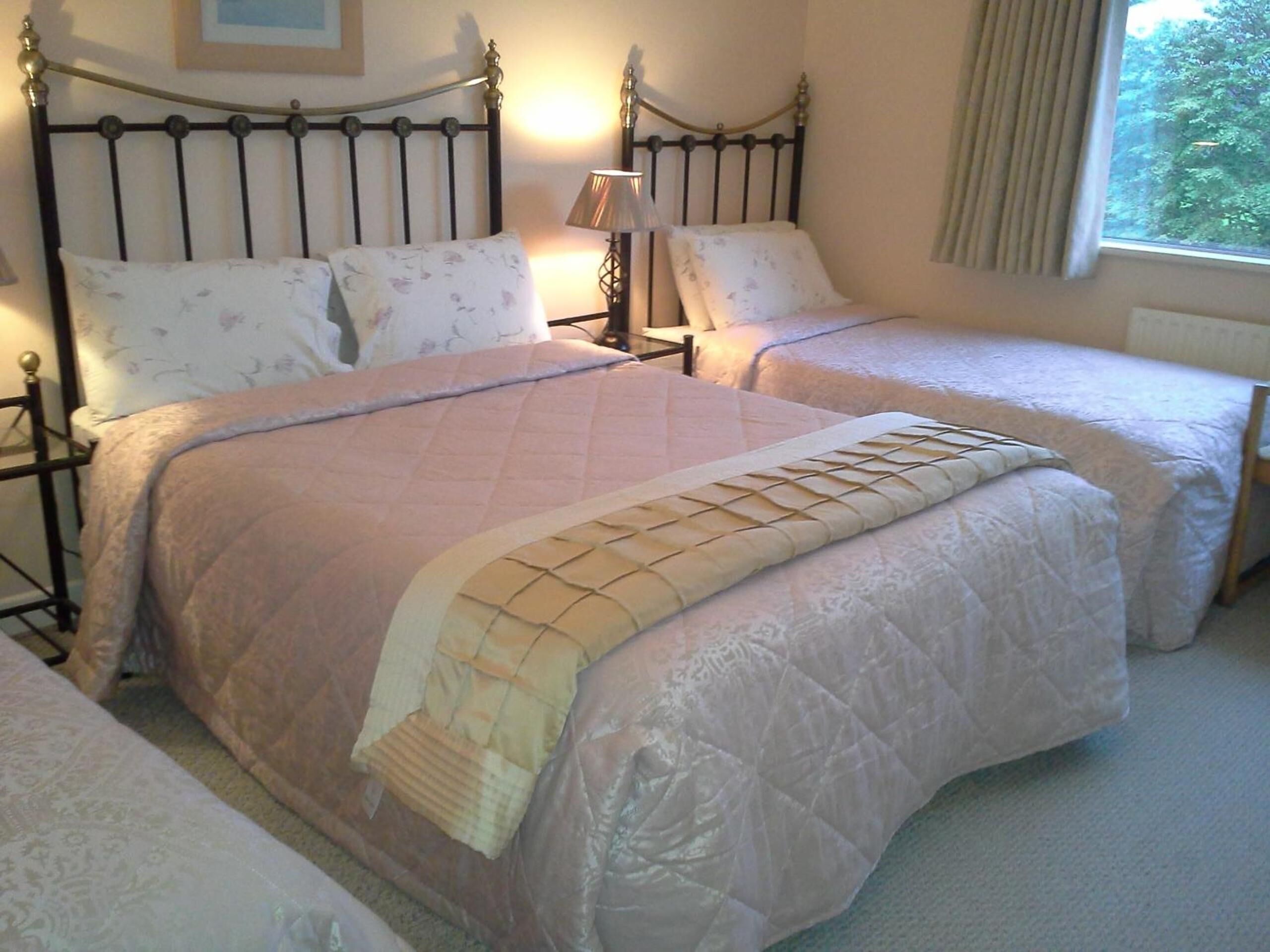 A bedroom with a double bed and two single beds, a bedside table with a lamp, and a window with curtains.