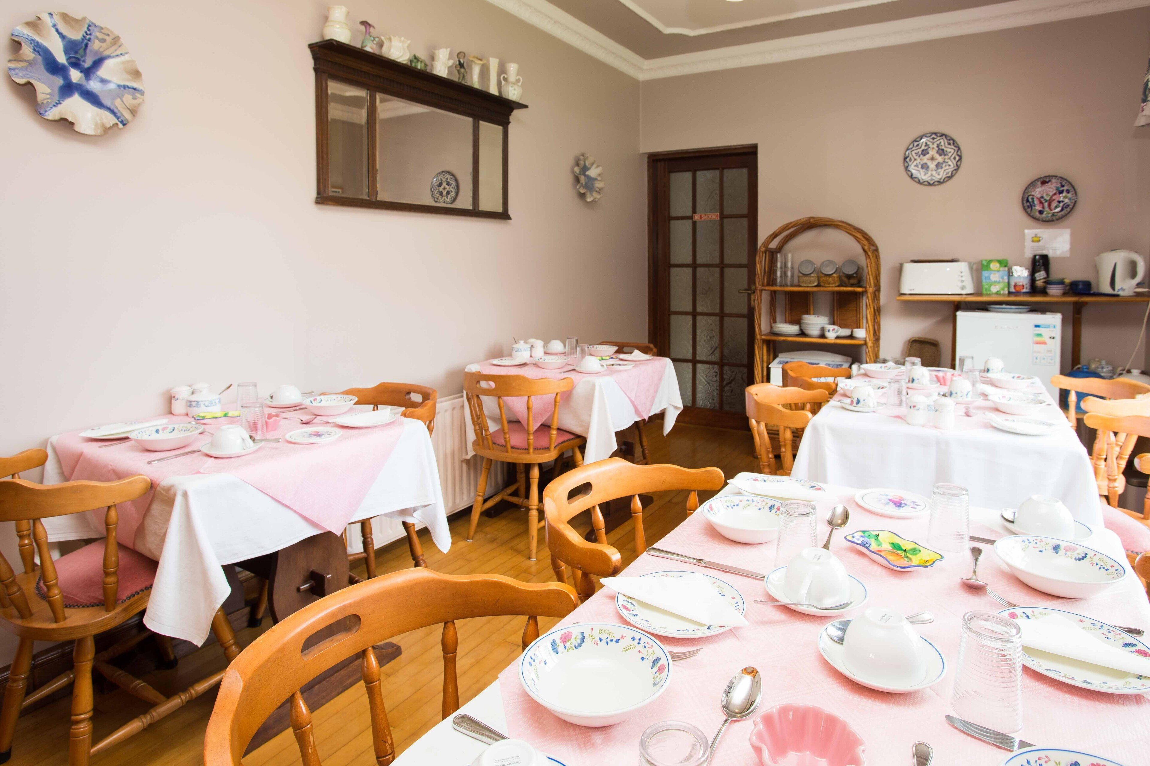 A dining area with multiple tables set for a meal, wooden chairs, and a kitchen area in the background.
