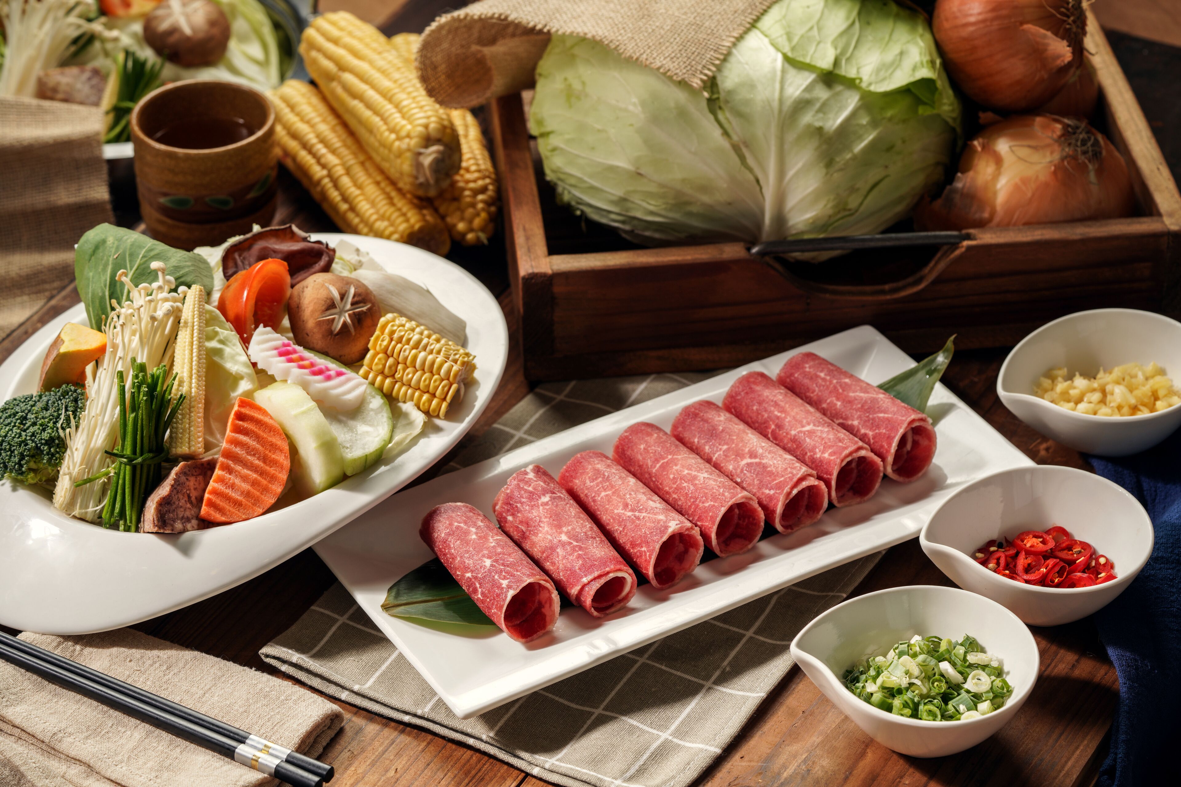 Diversos vegetais frescos e carne fatiada sobre uma mesa de madeira.