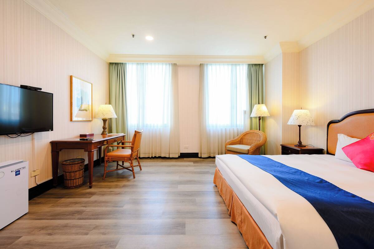 Ein Hotelzimmer mit Bett, Schreibtisch mit Stuhl, Fernseher und zwei mit Vorhängen versehenen Fenstern.