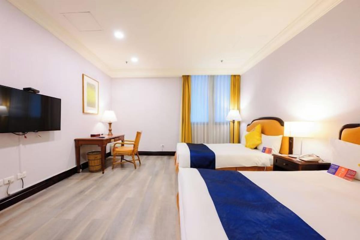 A hotel room with two beds, a desk, a chair, a television, and a window with curtains.