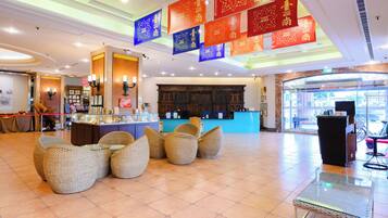 A hotel lobby with wicker furniture, a reception desk, and red banners with Chinese characters.