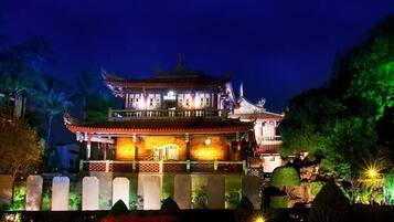 A traditional multi-tiered building with illuminated windows and a well-maintained garden at night.