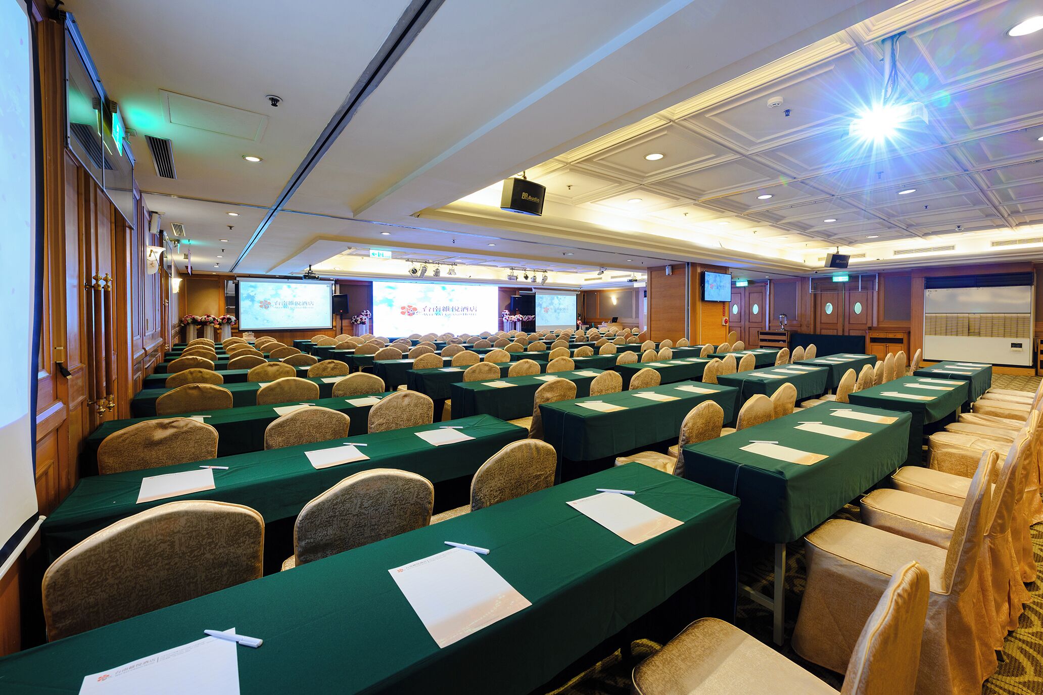A conference room with rows of tables and chairs, a projection screen, and a stage area.