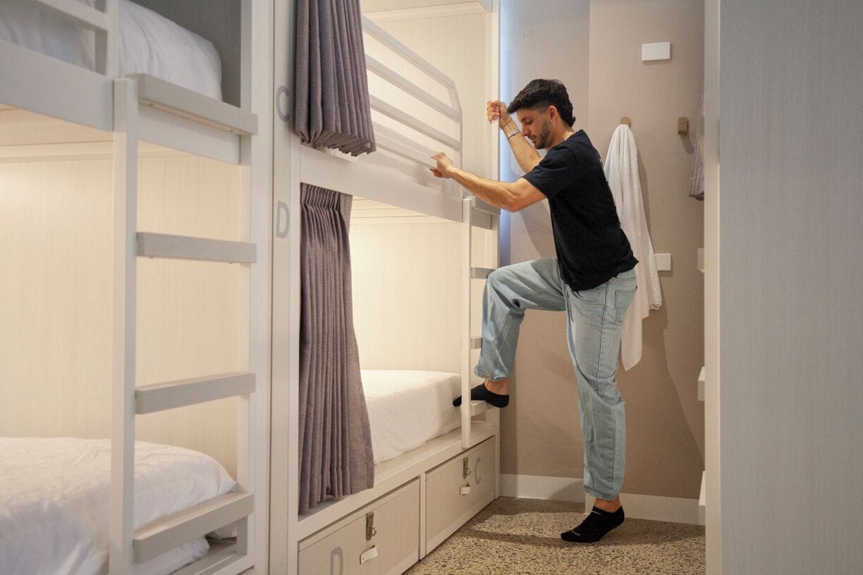 Une chambre avec un lit superposé, où une personne est en train de régler les rideaux.