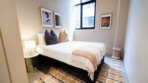 Un dormitorio ordenado con cama, lámpara de noche y cuadros en la pared.