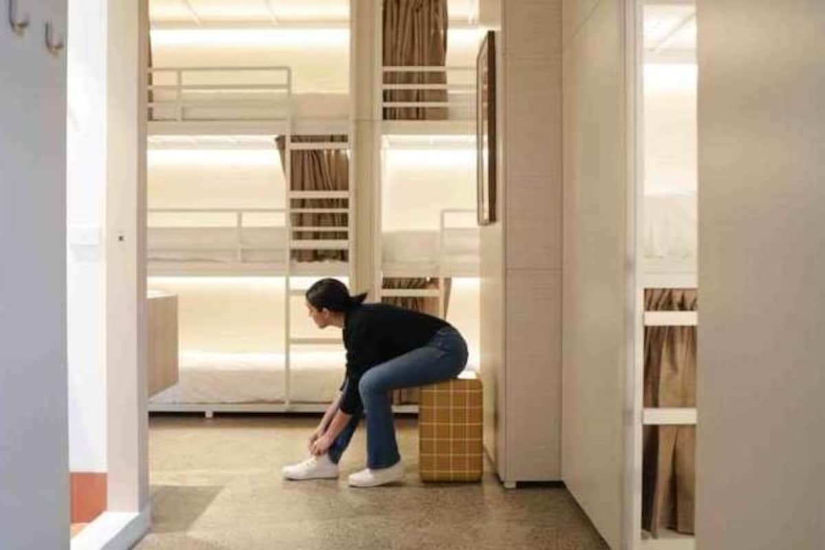 A person adjusting a suitcase in a hotel room with bunk beds and a wardrobe.