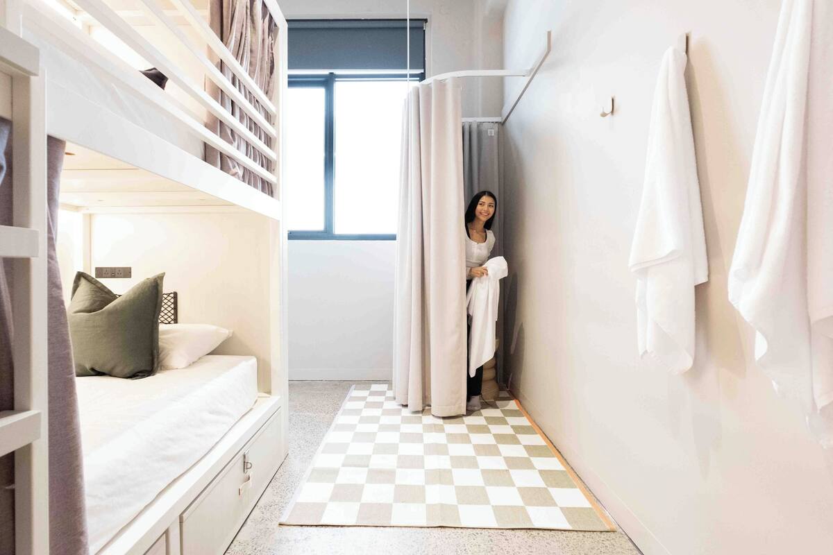 A hotel room with a bunk bed, a checkered rug, a shower curtain, and towels on the wall.