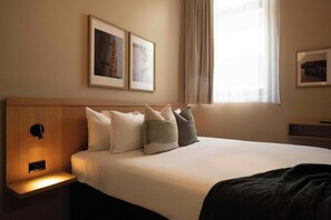 A hotel room with a bed, pillows, a nightstand, a wall-mounted light, and framed pictures. - Little Drifter Melbourne (Melbourne)