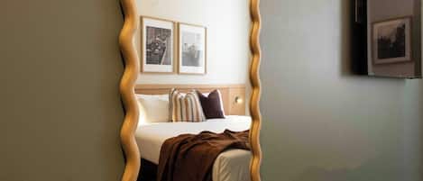 Un dormitorio con cama, almohadas, una manta y dos cuadros en la pared.