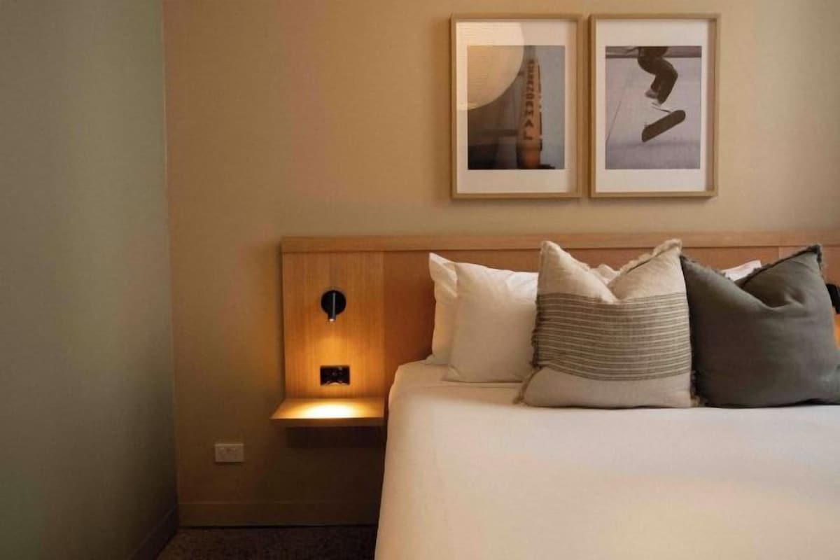 A hotel room with a bed, a nightstand, and two framed pictures on the wall.