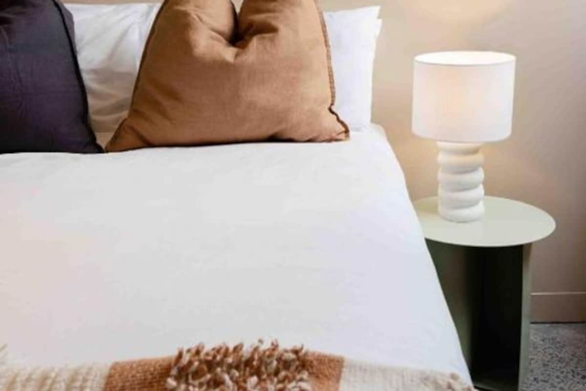 A hotel room with a bed, pillows, a nightstand with a lamp, and two framed pictures on the wall.